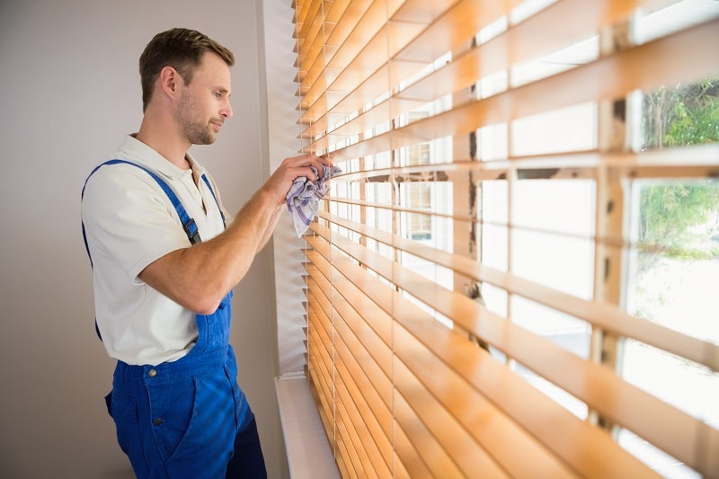 man cleaning window blind panels