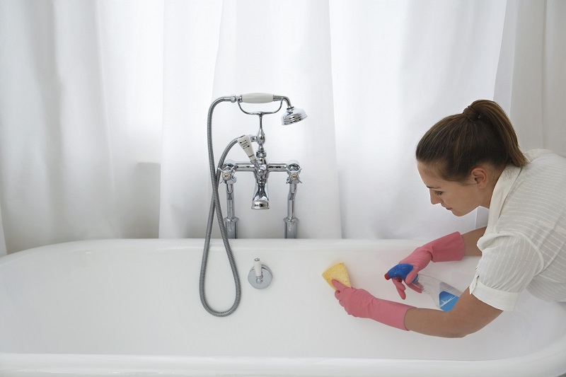 woman cleaning bathtub with sponge and spray