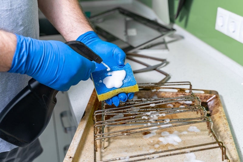 man cleaning dirty oven grills and trays