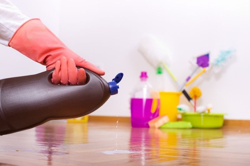 Person's hand holding a cleaning bottle with cleaning products at the back