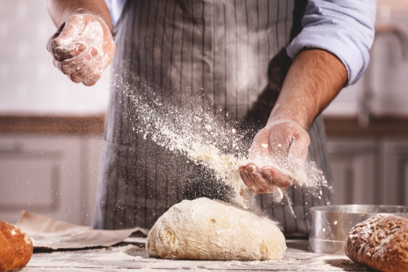 baker putting flour on dough