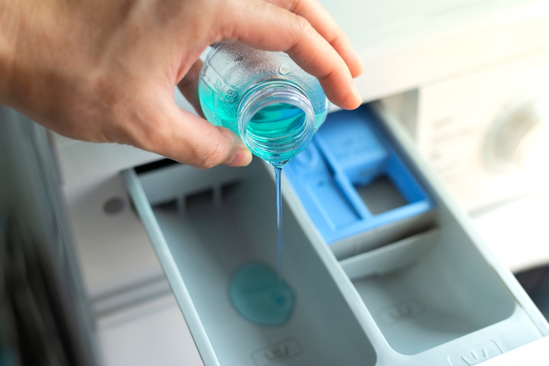 hand pouring liquid detergent in washing machine drawer