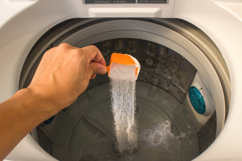 hand pouring detergent powder to washing machine drum
