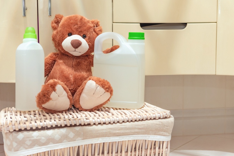 brown teddy bear on laundry basket with detergent bottles